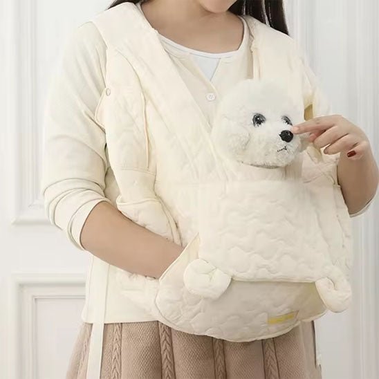 Une personne portant un gilet de couleur crème tient un sac de transport pour chien ventral blanc, à l'intérieur duquel un petit chien blanc est confortablement assis.